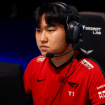 Jugador profesional de T1 en una partida de LCK, concentrado frente al monitor, usando audífonos con micrófono y camiseta roja del equipo.