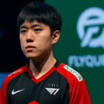 Jugador de T1 concentrado en el escenario de Worlds 2025 con el logo de FlyQuest de fondo y luces de torneo
