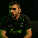 Retrato reflexivo de ATF, jugador de Team Falcons, iluminado por luces verdes y moradas tras ganar TI 2025.