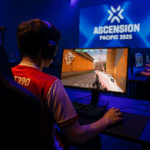Jugador compitiendo en el torneo VCT Ascension Pacific 2025 en Bangkok, concentrado frente a su monitor en un escenario iluminado.