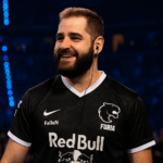 FalleN sonríe en el escenario con la camiseta de FURIA durante un torneo de CS2, bajo luces azules y doradas.
