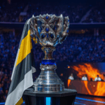 La Copa del Invocador en el escenario del Worlds 2025, rodeada de luces azules y doradas, con jugadores compitiendo y público en un estadio lleno.