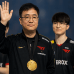 Entrenador coreano KkOma levantando la mano con medalla de campeón, frente a sus jugadores de T1 en un escenario de esports.
